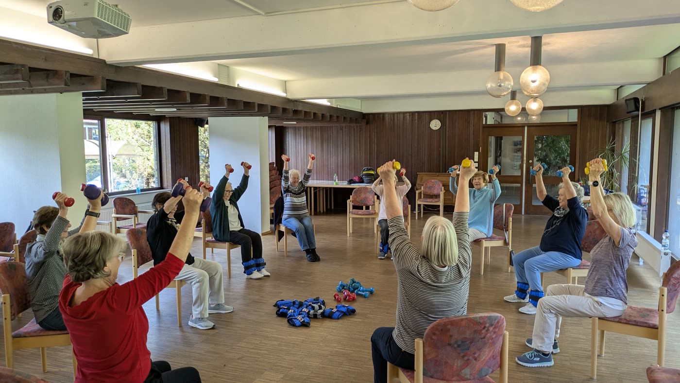 Die Gruppe streckt beim Training gemeinsam die Hanteln nach oben